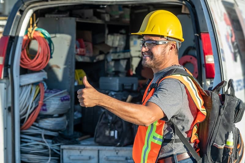 Smiling hispanic construction worker wearing a work helmet looking away with his thumbs up-cm