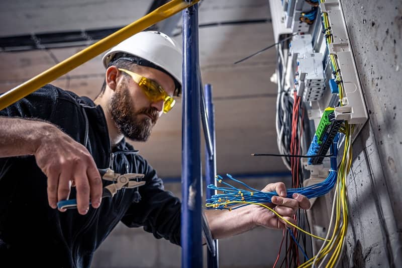 A male electrician works in a switchboard with an electrical connecting cable-cm
