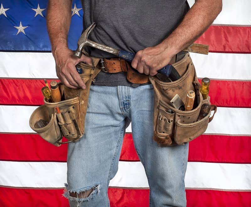 Carpenter wearing leather tool belt with hand tools in front of American flag-cm