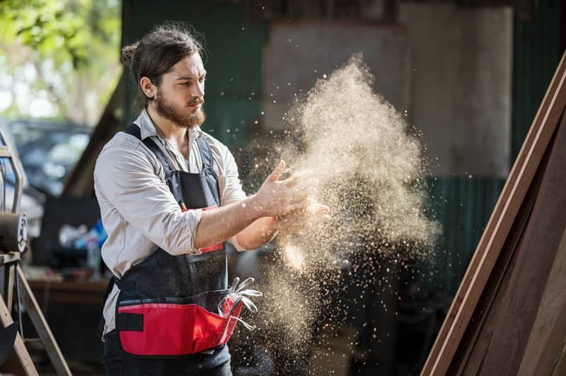 Woodworker cleaning wood dust from his gloves by clapping hands in the wood workshop-cm