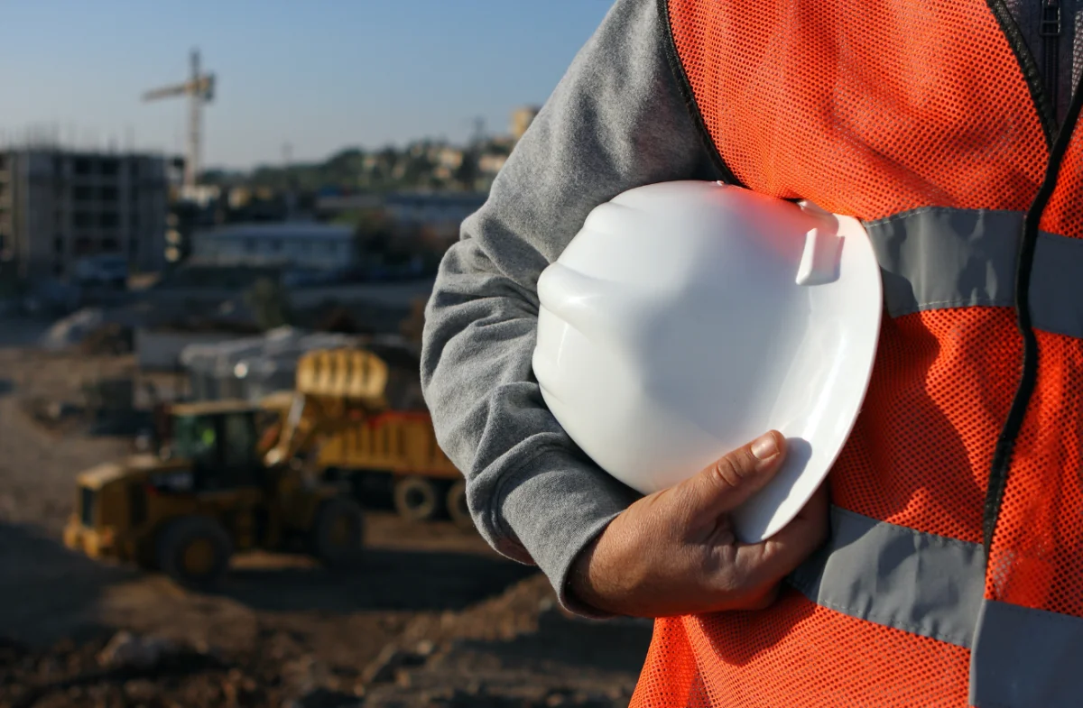 Construction worker holding a white hard hat on an active job site representing industrial and construction staffing services across the United States.